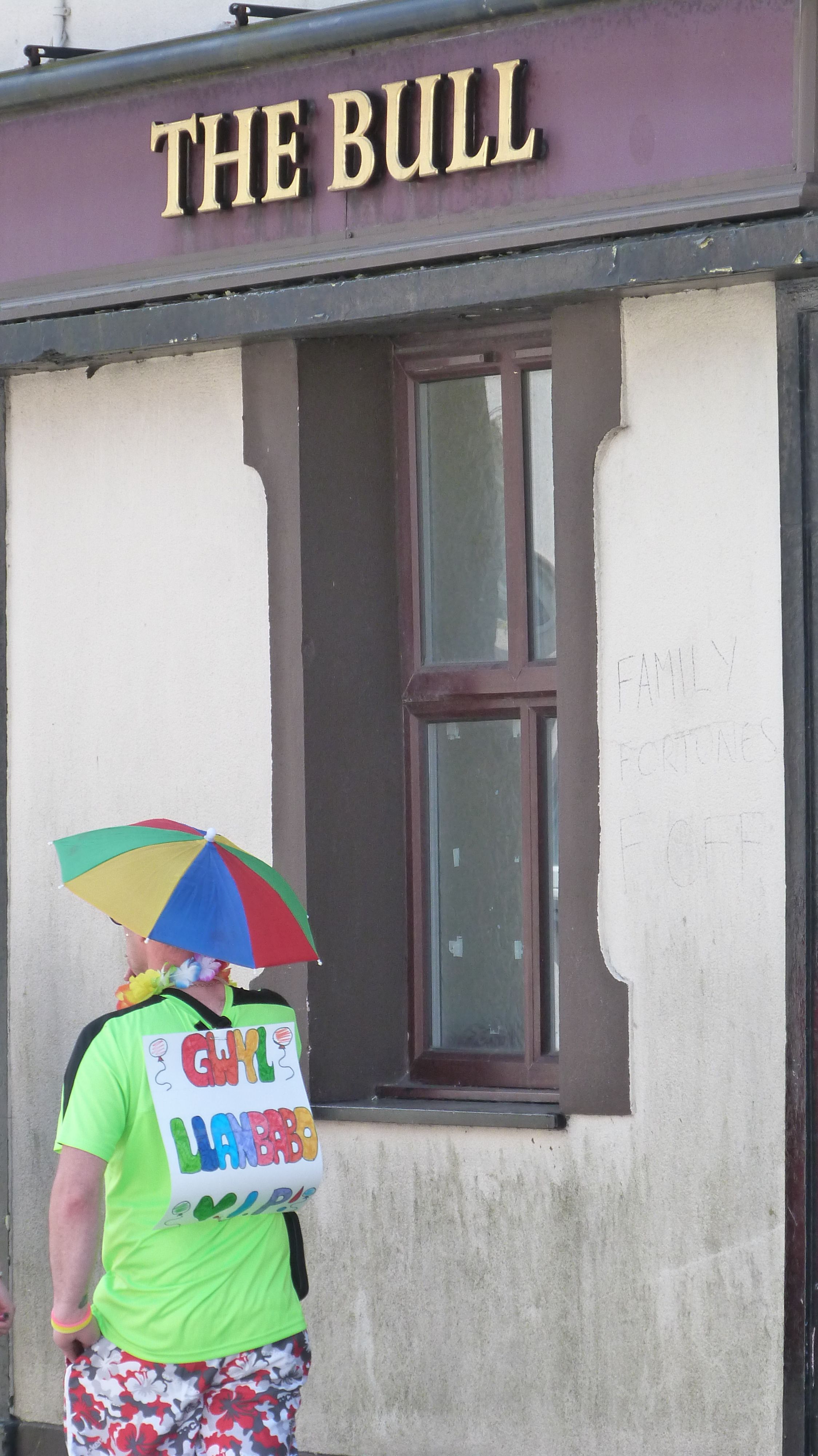 Dyn mewn gwisg ffansi yn cerdded heibio i dafarn wedi cau