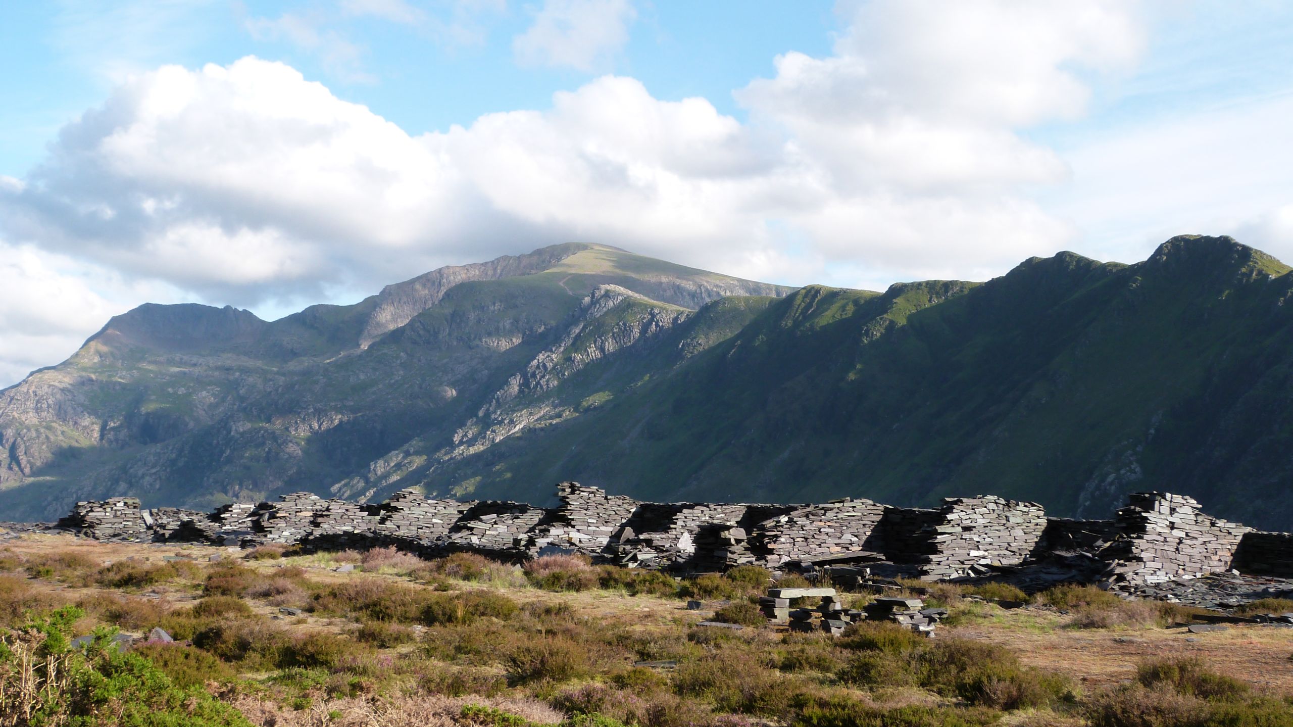 Gweddillion gweithfeydd gyda Crib Goch a mynyddoedd Eryri yn y cefndir