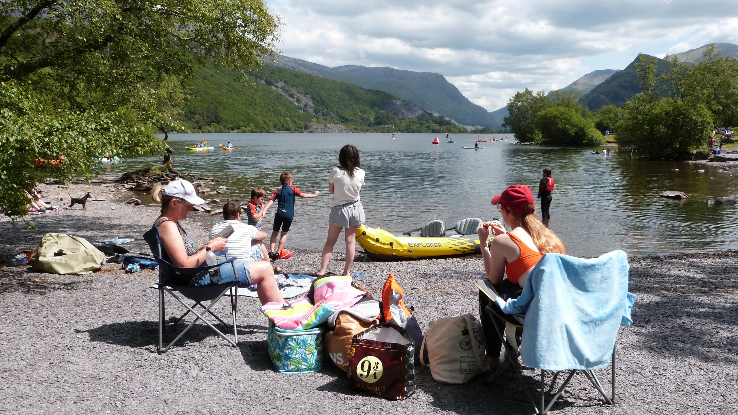 Llyn Padarn ar ddiwrnod braf gyda pobl yn cael picnic ar y lan a nifer o gychod ar y dŵr