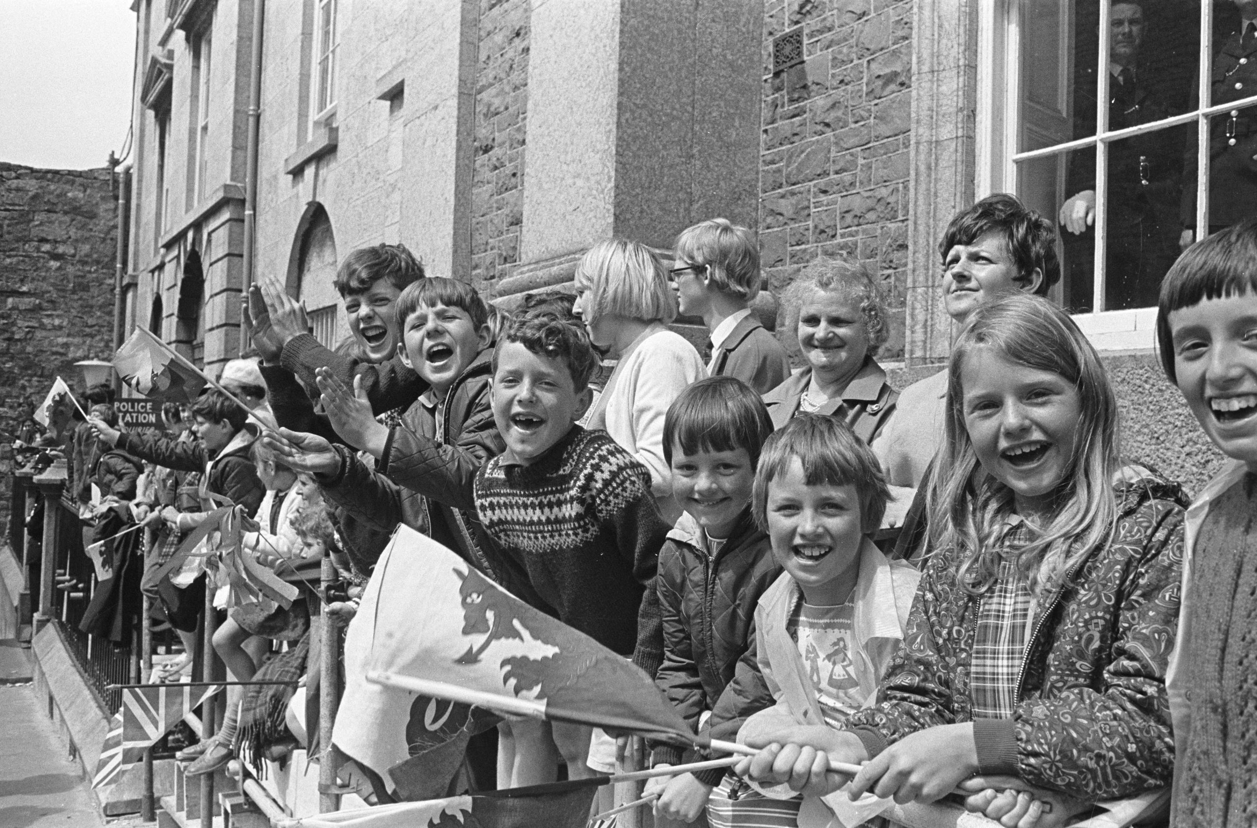 Criw o blant ac oedolion yn dathlu gyda baneri ger y Catell