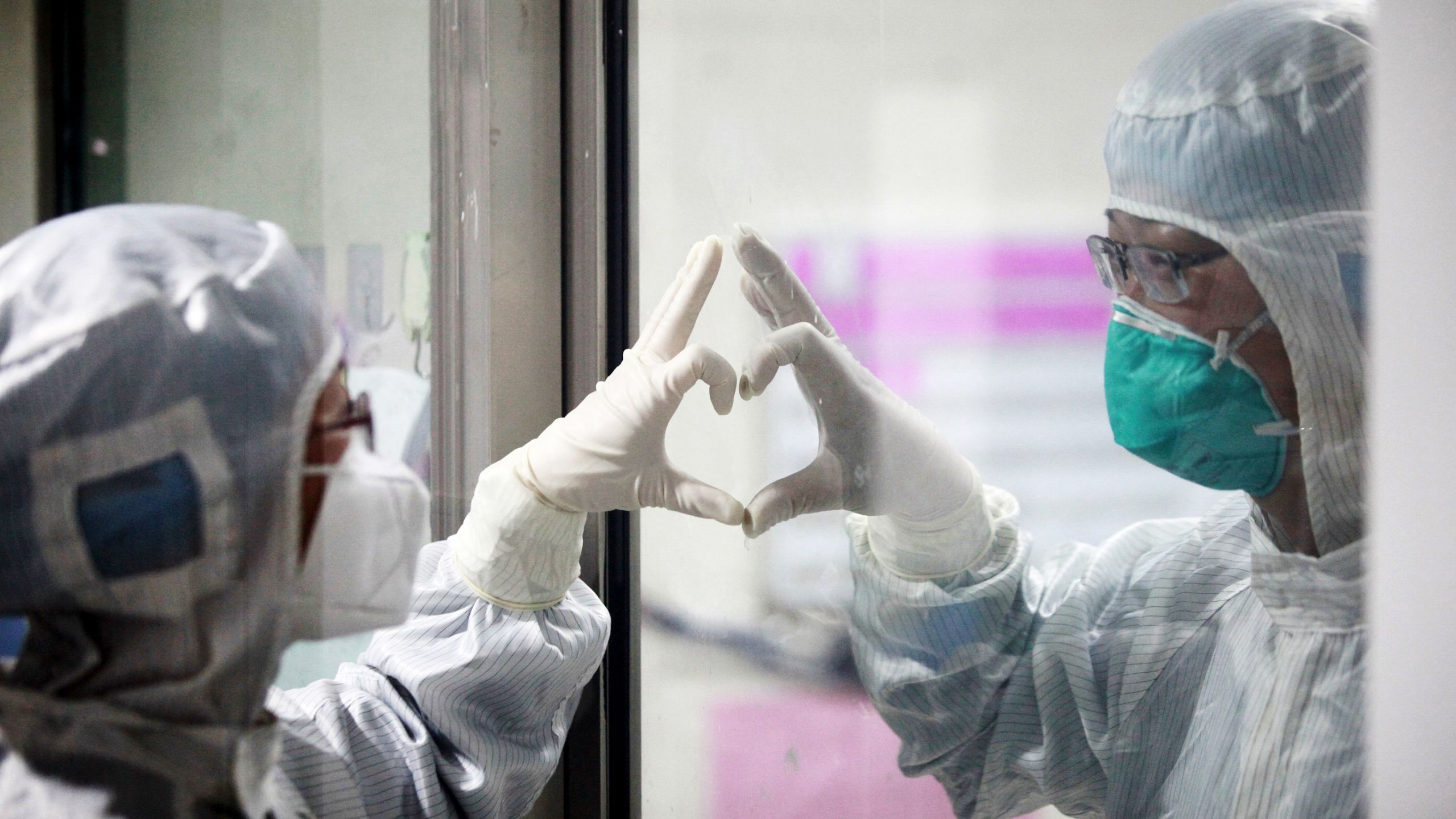 Two medical workers in China make a heart symbol to each other through a window for protection
