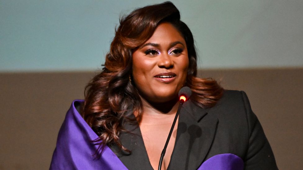Danielle Brooks where‍‍`s black and purple in front of a podium and microphone