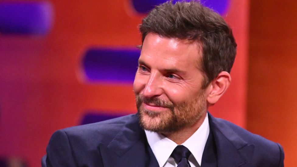 Bradley Cooper wears a suit and smiles