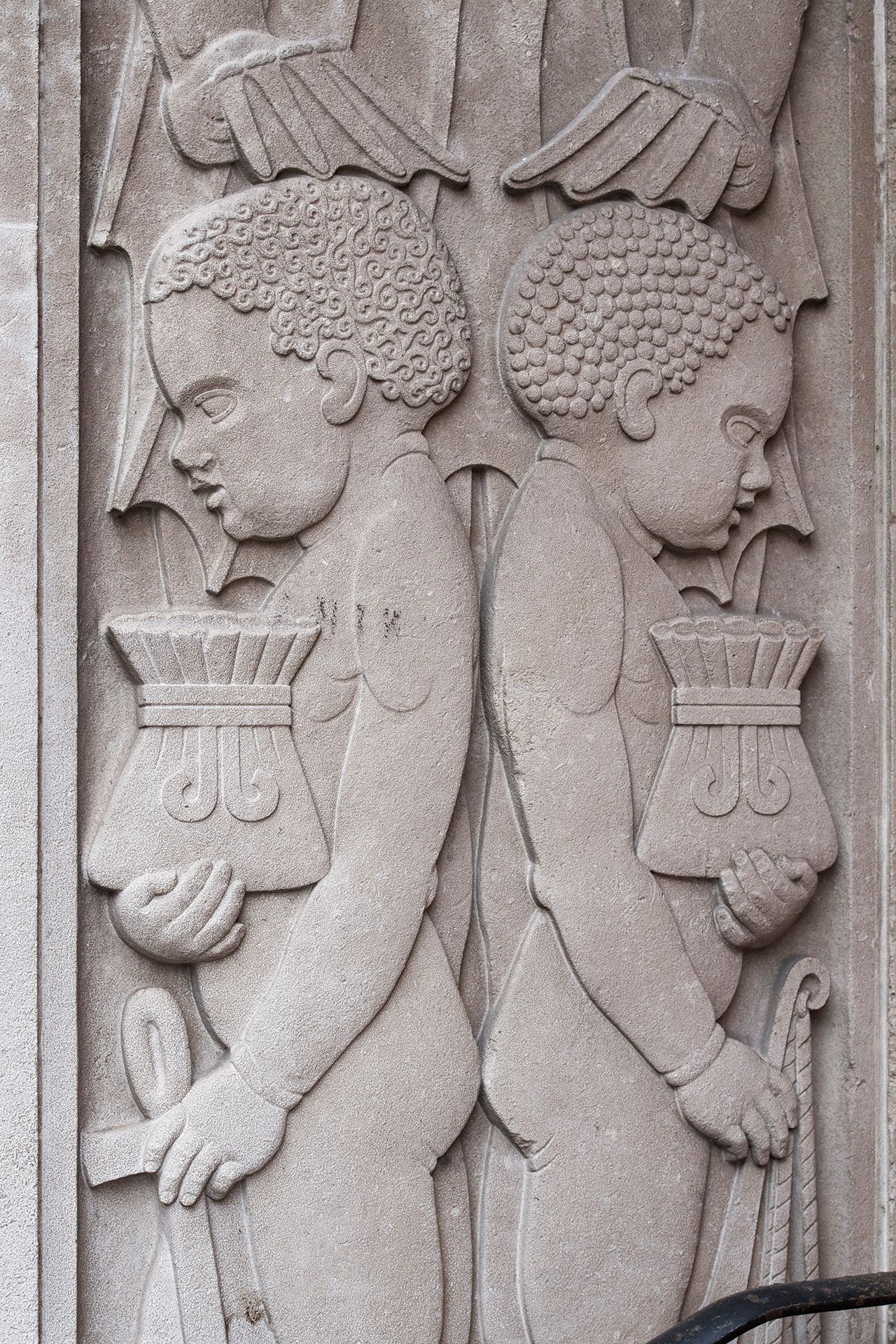 Relief sculpture of two black boys in profile, holding pots of gold