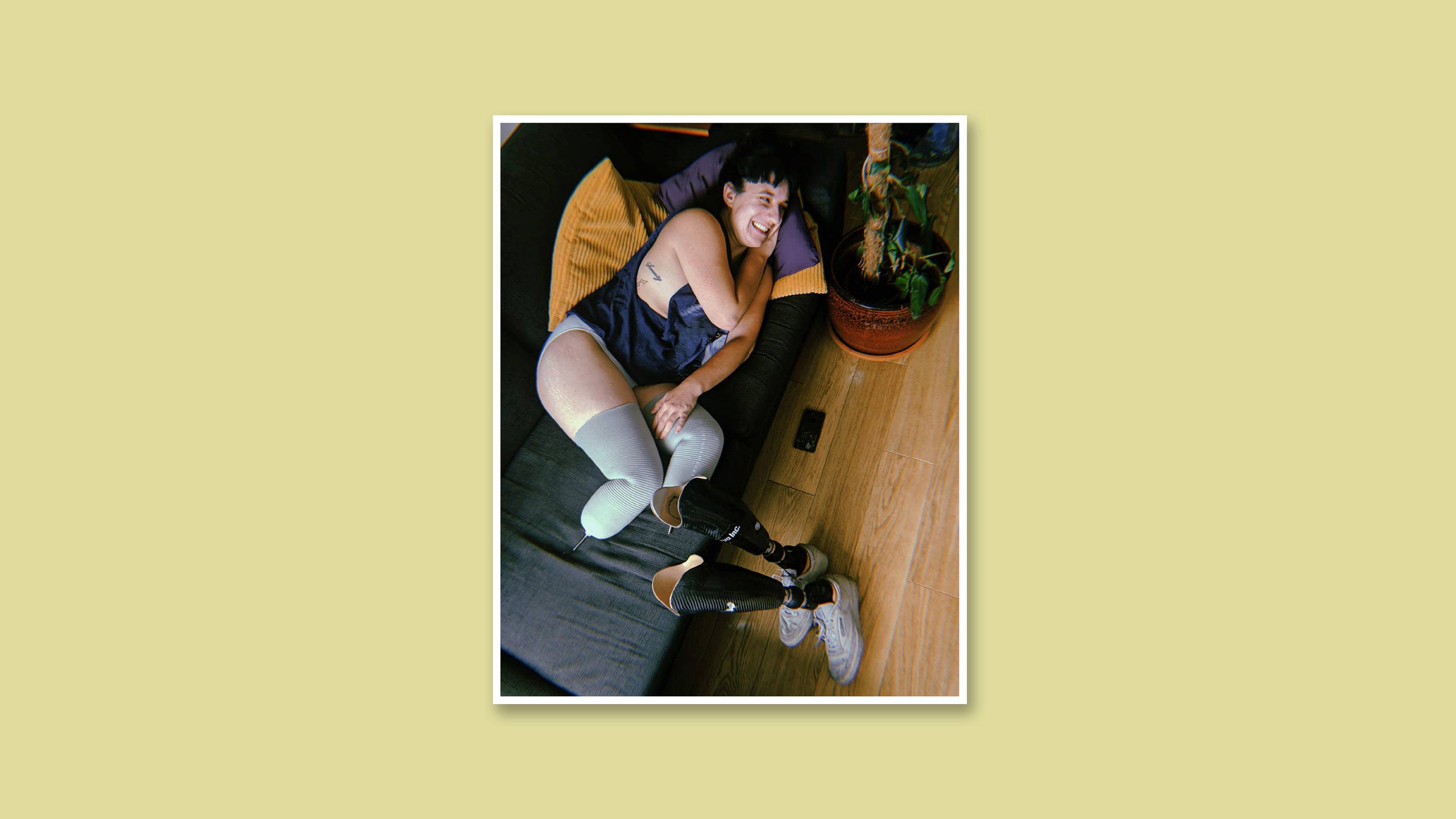 Kat laying on a sofa, smiling, with her prosthetics on the floor