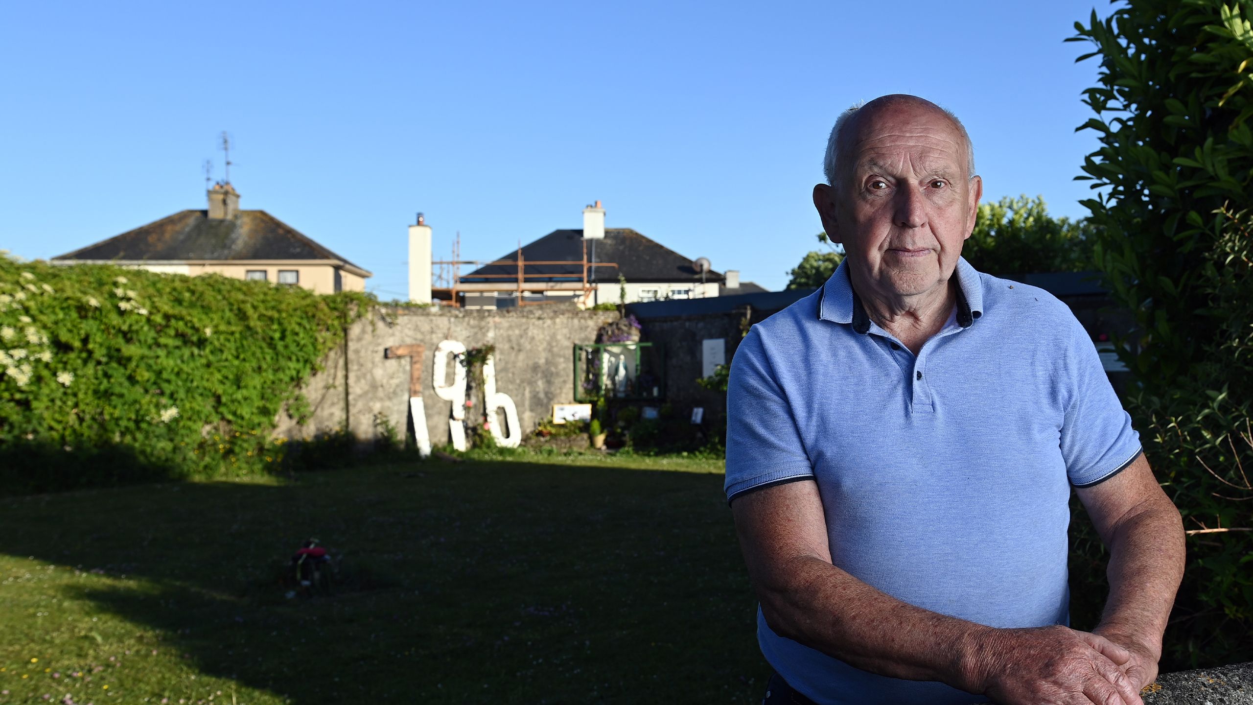 PJ Haverty pictured in the sunlight at the memorial garden in Tuam. There is a wall in the background with a memorial and a large number 796.