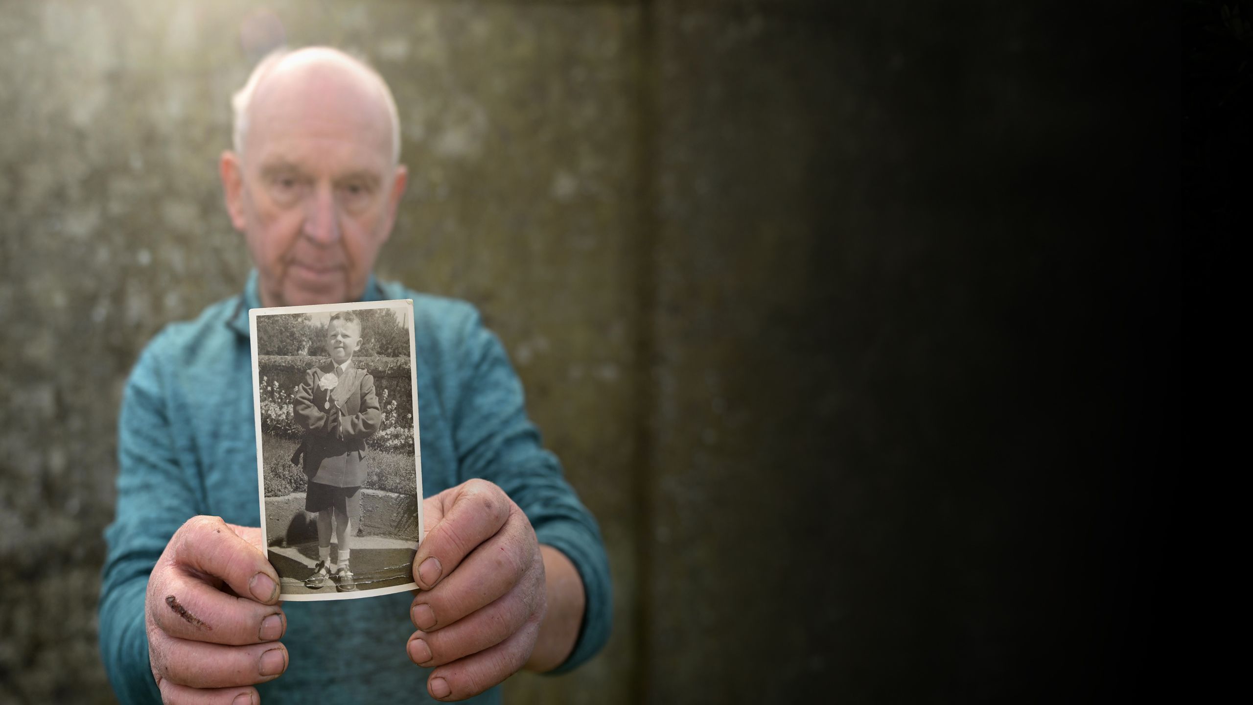 PJ Haverty holding up a picture of him when he was a young boy. He is shown wearing a school uniform with his arms folded.