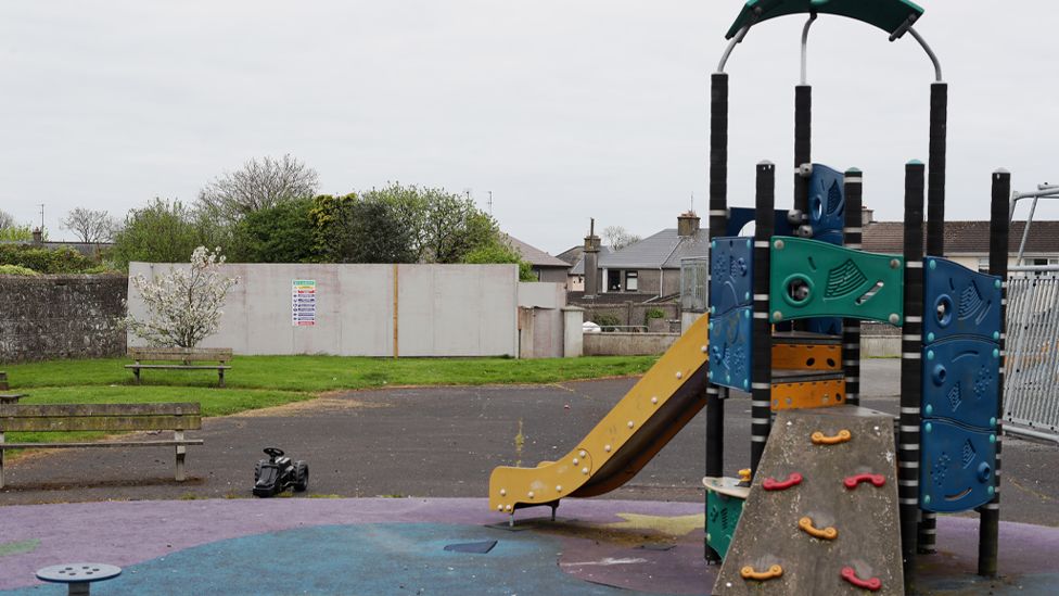 Image of the playground on the site of the excavation. It shows a climbing frame and a yellow slide, with a fence in the background showing the closed off area of the site ahead of excavations.