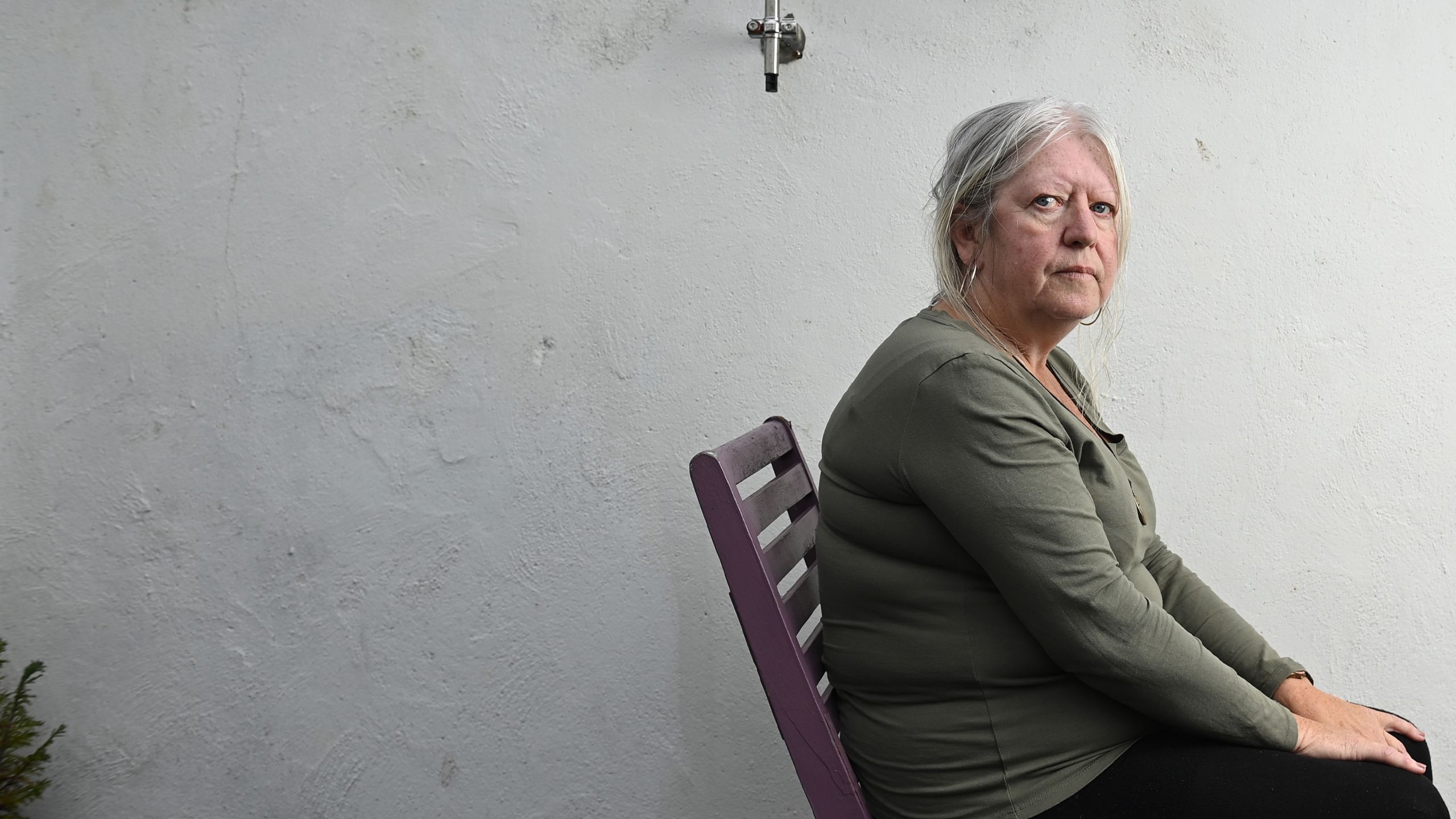 Anna Corrigan pictured against a white wall looking directly into the camera. She is wearing a dark green top sitting on a chair.
