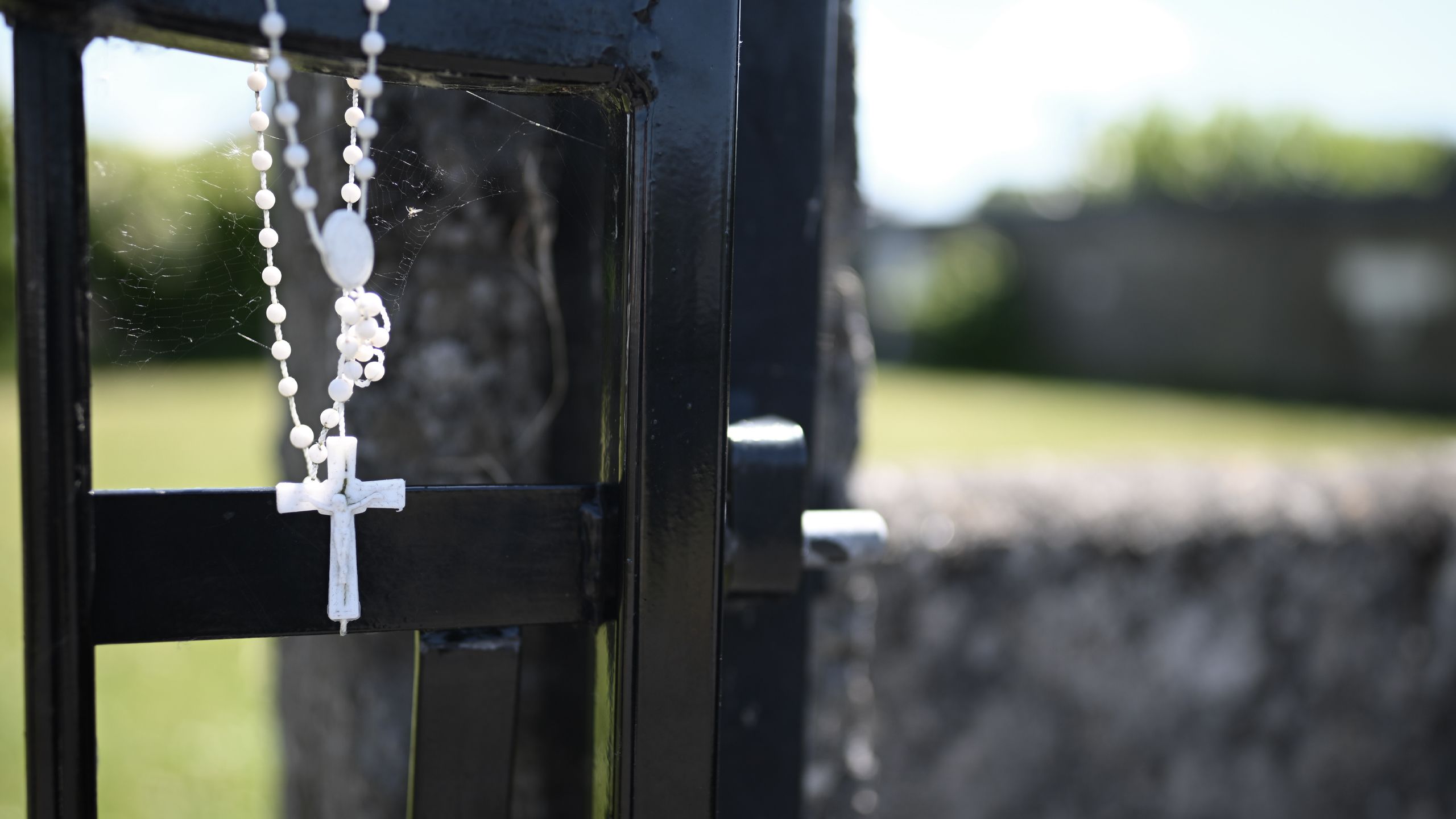 Picture of showing the gated entrance to the memorial site, with a white rosary beads hanging off the gate.