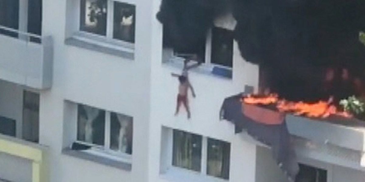 Child dangling precariously from a window as a fire rages