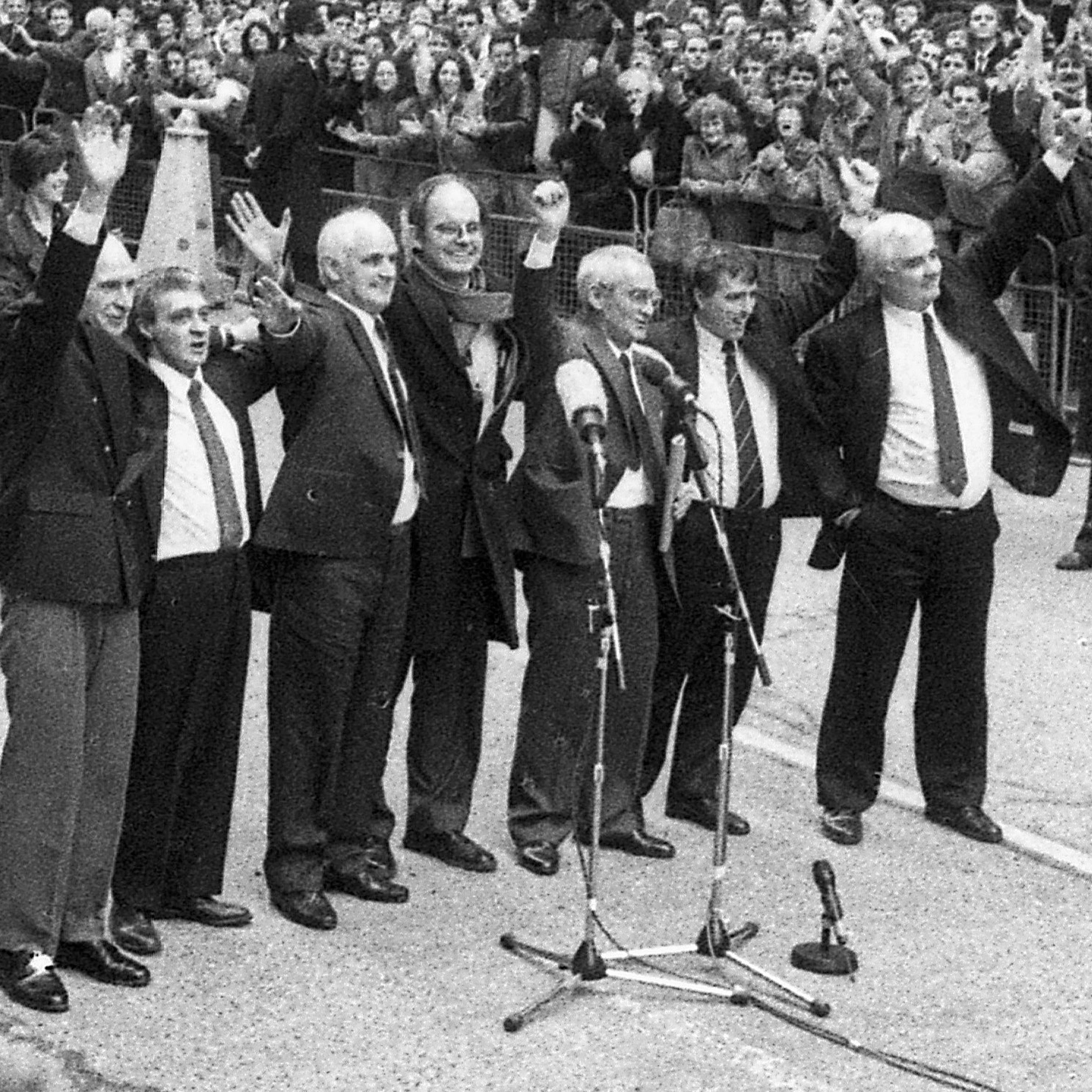 A black and white image of the Birmingham Six and campaigner Chris Mullin celebrating their release in 1991. They stand in a line with arms raised in celebration