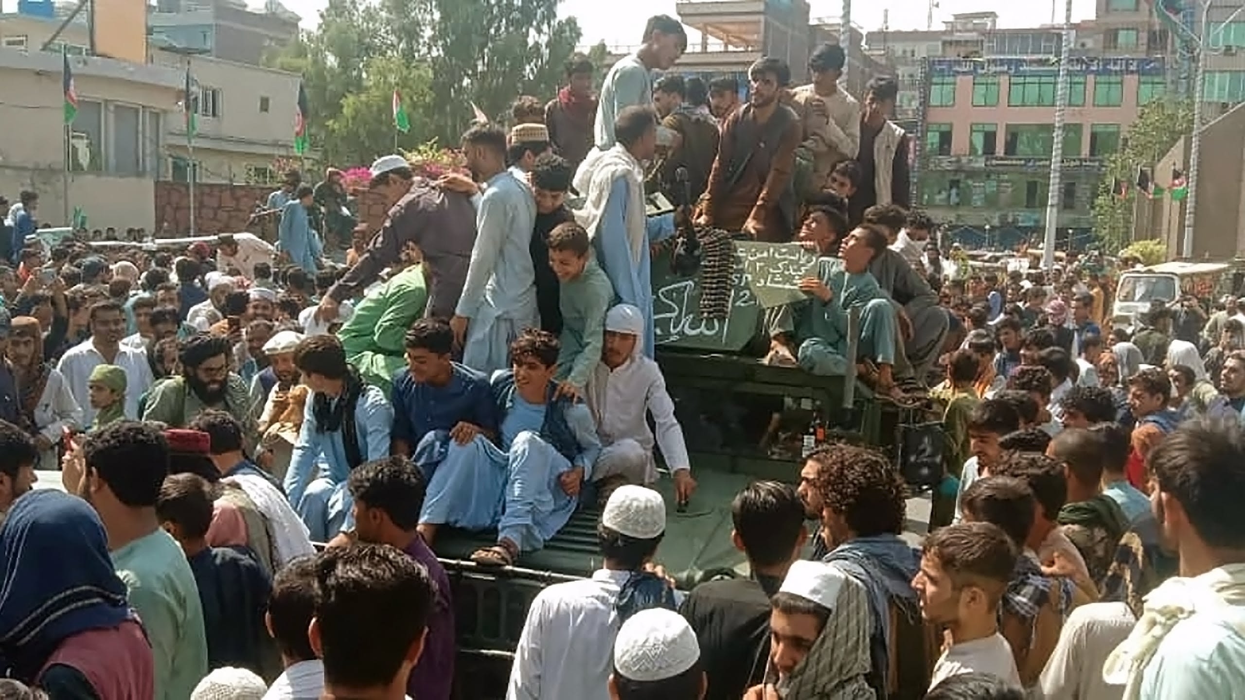 Taliban fighters and local people sit on an military vehicle Afghan on a street in Jalalabad