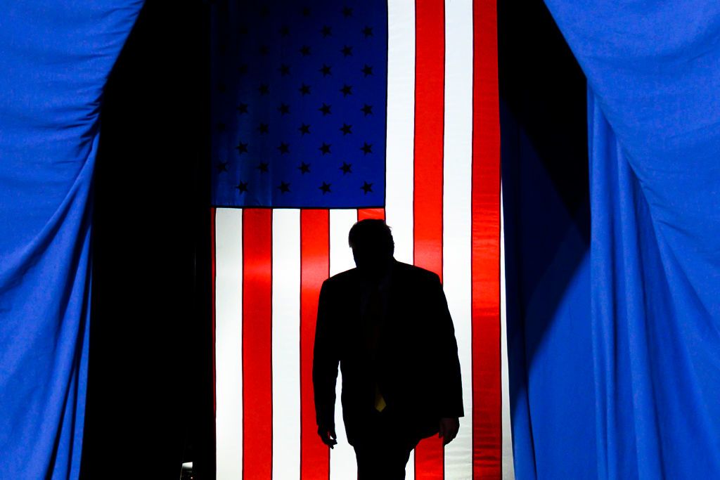 Donald Trump caminha de costas com a bandeira americana ao fundo