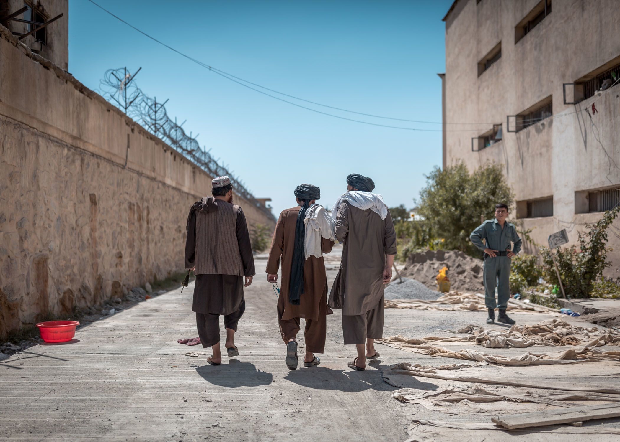 Three Taliban elders walk around the prison perimeter