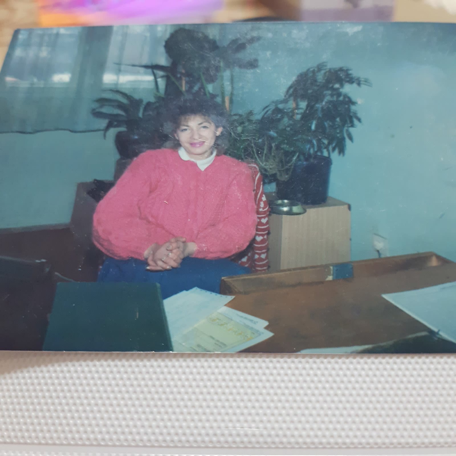 Fotografija iz mladosti, od pre rata, Rehana sedi za stolom, spojenih ruku, nasmejana