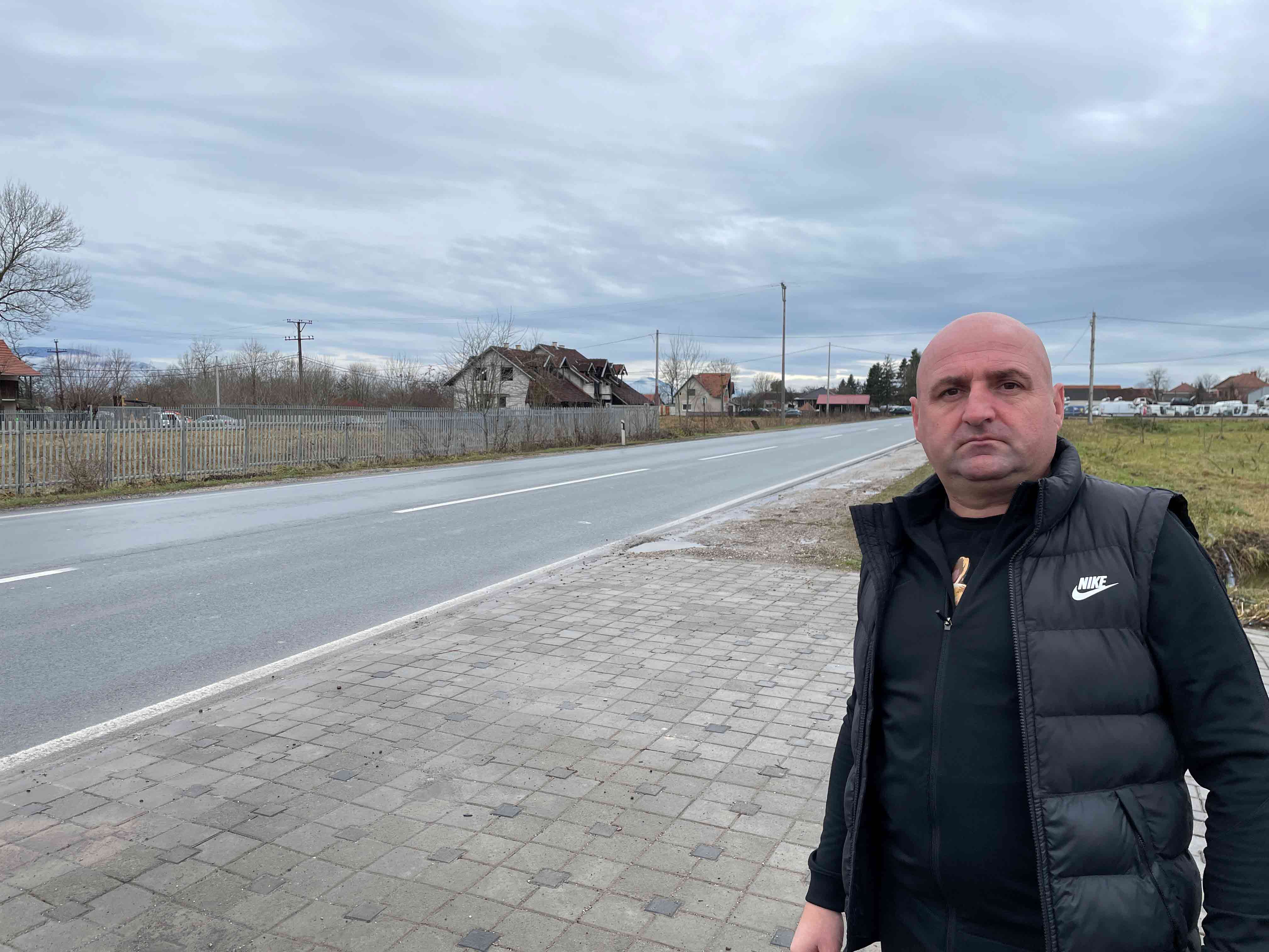 Na slici je Ivan Grbić, srednjih godina, ćelav, okruglasto lice, nosi crni prsluk. On je u desnom polju fotografije, levo je put koji nestaje u daljini.