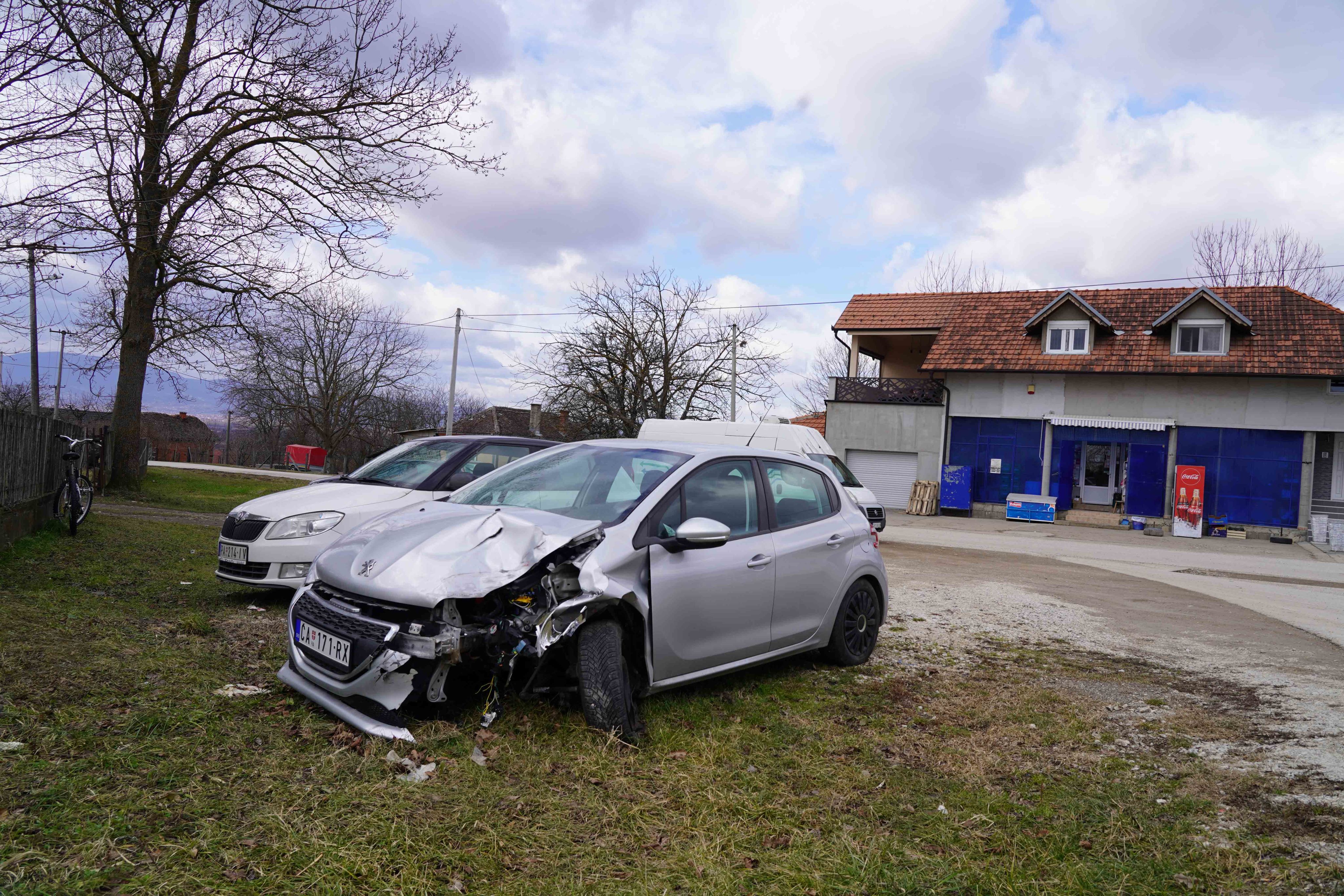 Parkirani automobil, slupan, u Mojsinju, u pozadini je seoska prodavnica
