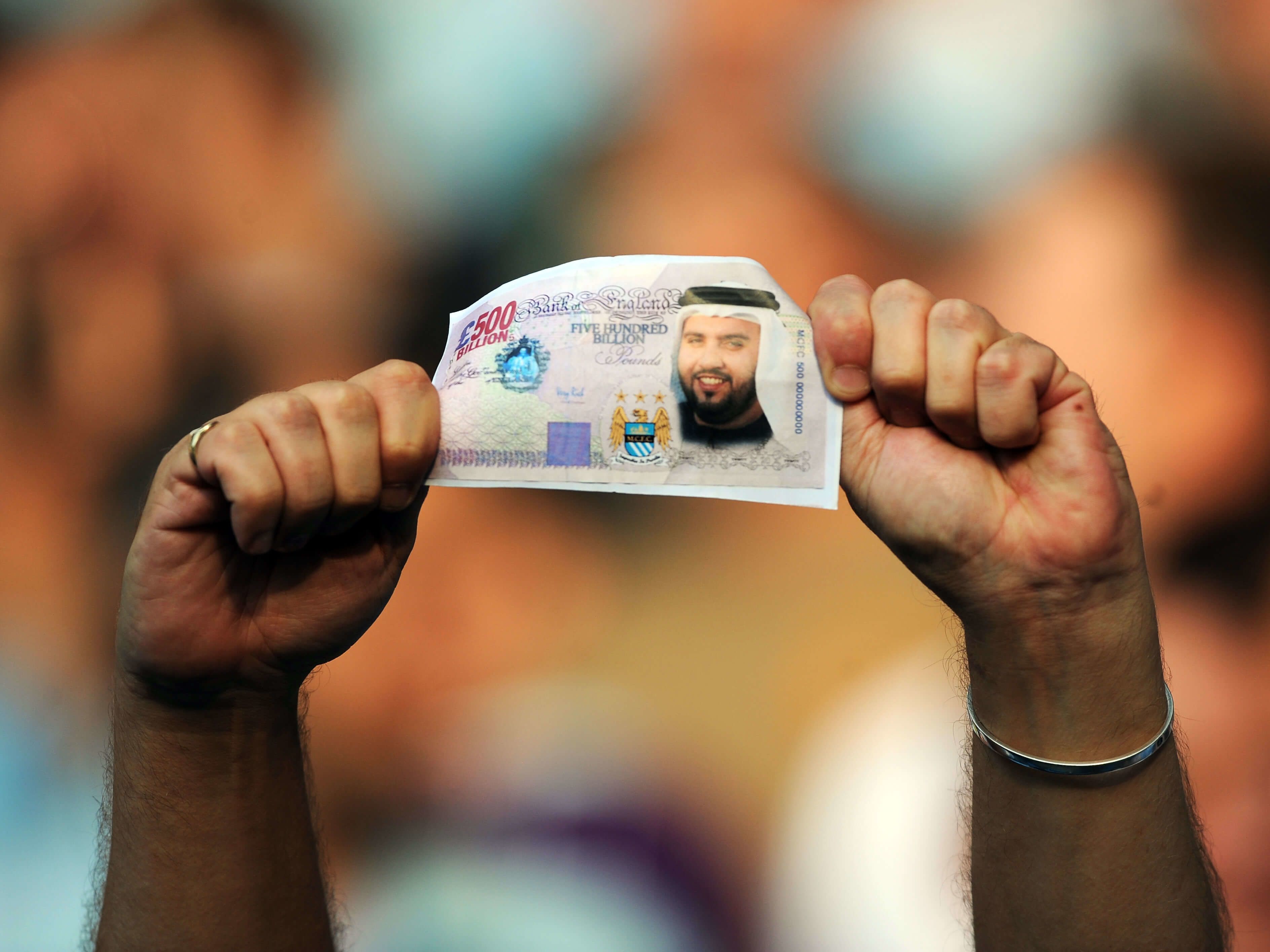 A Manchester City fan holds a fake British Pound note with the face of Dr Sulaiman Al Fahim