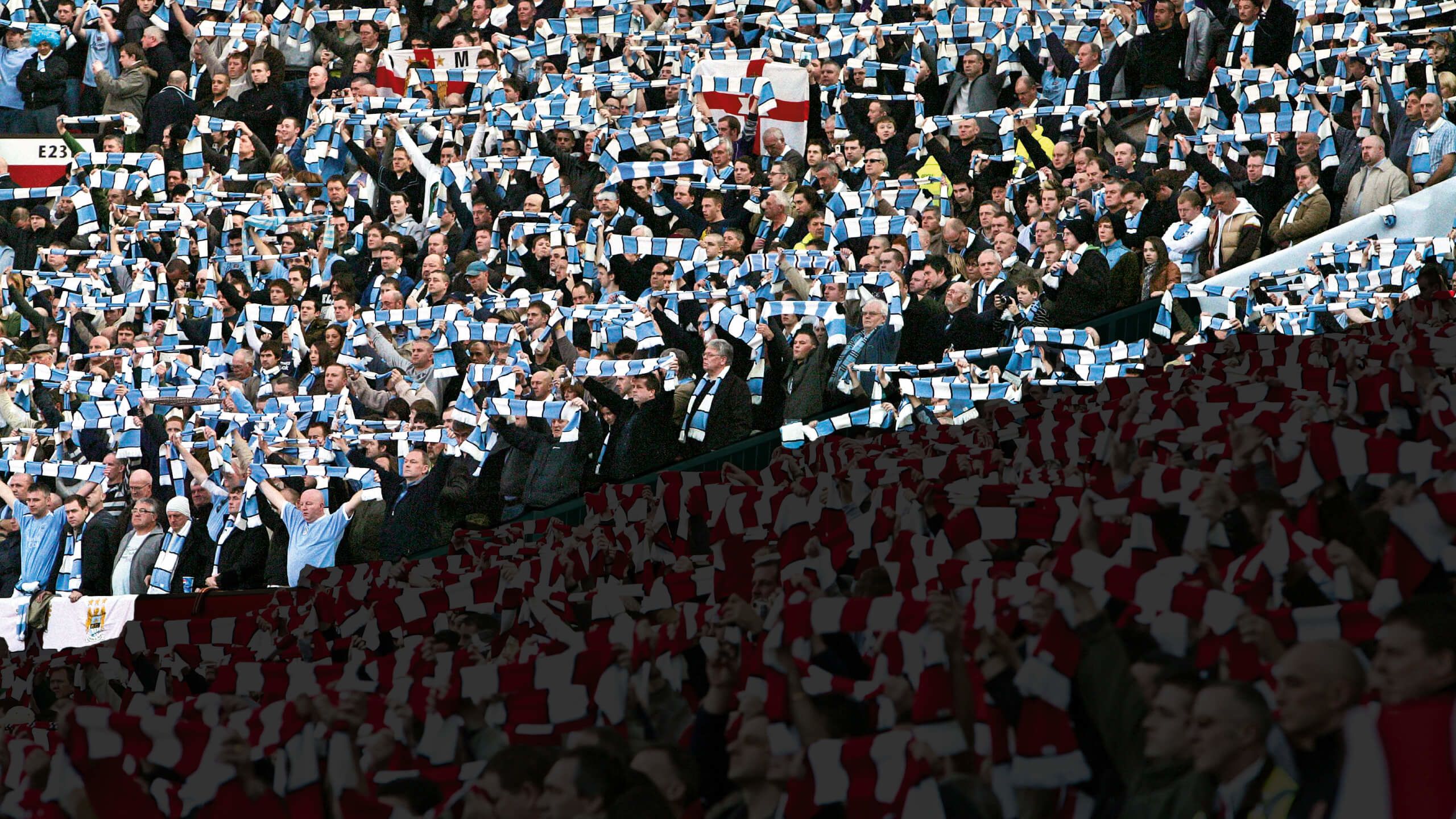 Manchester City (blue) and Manchester United (faded out) hold aloft scarves in remembrance of those who lost their lives in the Munich air disaster