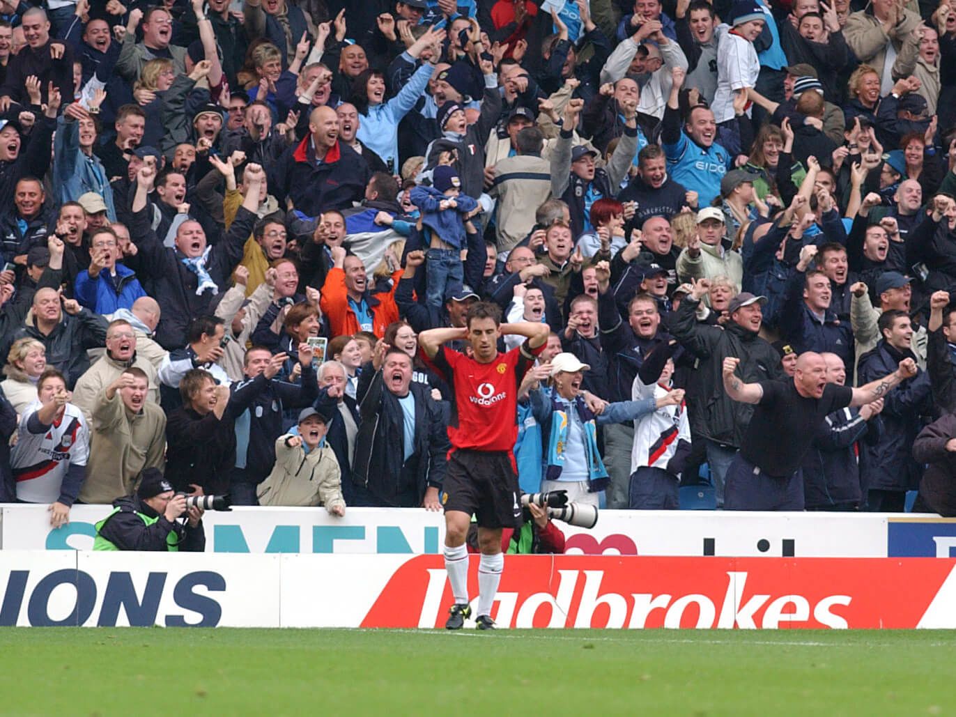 City fans celebrate as Gary Neville holds his head in his hands after his mistake to let Shaun Goater score in a 2002 Manchester derby