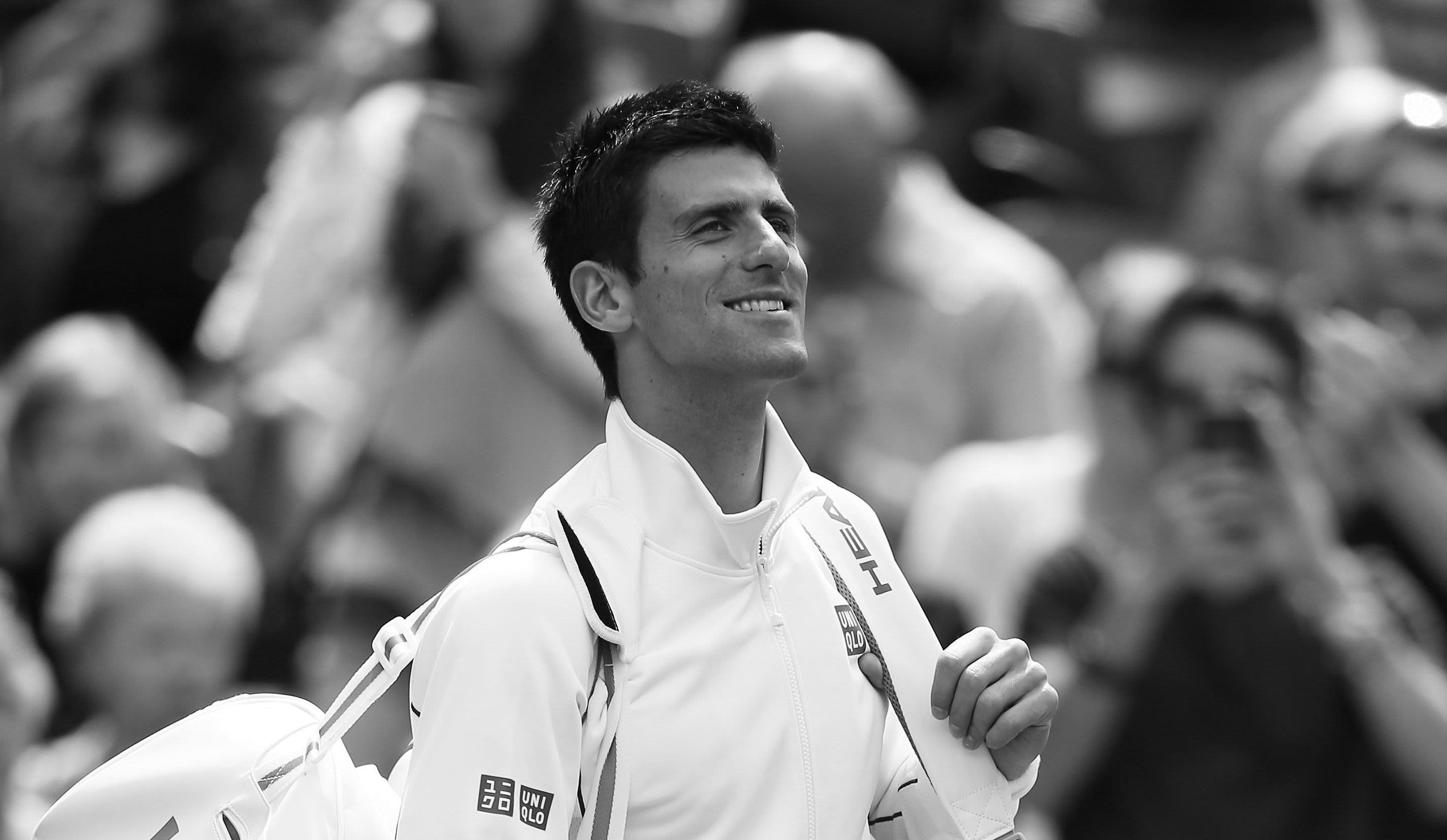 Novak Djokovic smiles as he carries his bags onto Centre Court