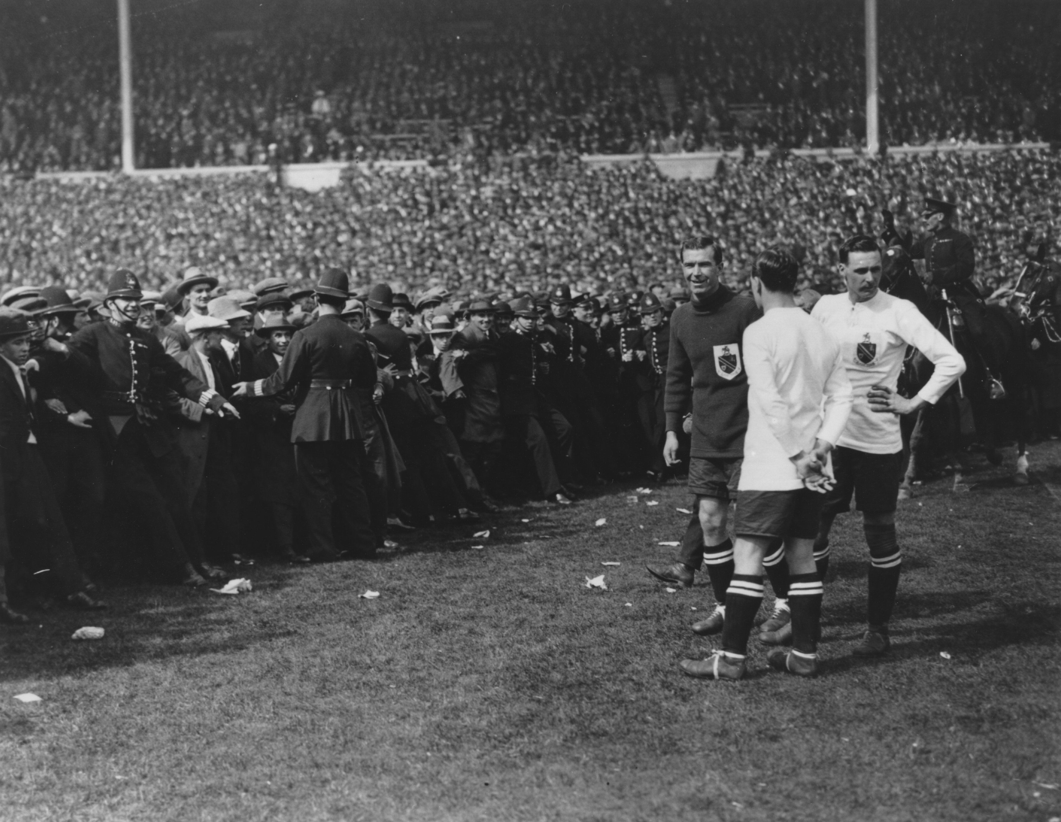 West Ham players on the pitch as police push crowds back at the 1923 FA Cup final