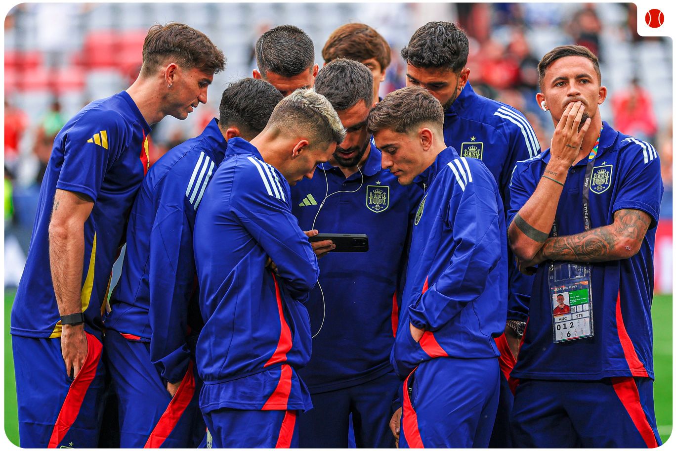 Spanish football players in team tracksuits gather closely around a mobile phone, watching the French Open final.