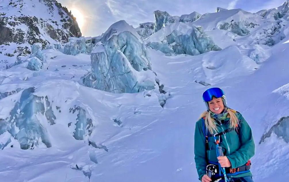 Chemmy standing on a snowy glacier surrounded by tall, jagged ice formations, with sunlight glowing behind the nearby mountain ridge