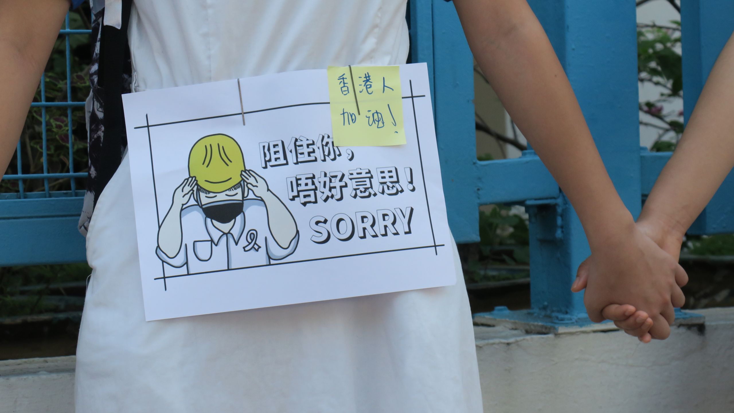 香港新界元朗大球場外一名參與「反送中」人鏈抗議的女中學生在校服上張貼「抱歉擋路」標語牌（9/9/2019）（BBC News中文圖片）