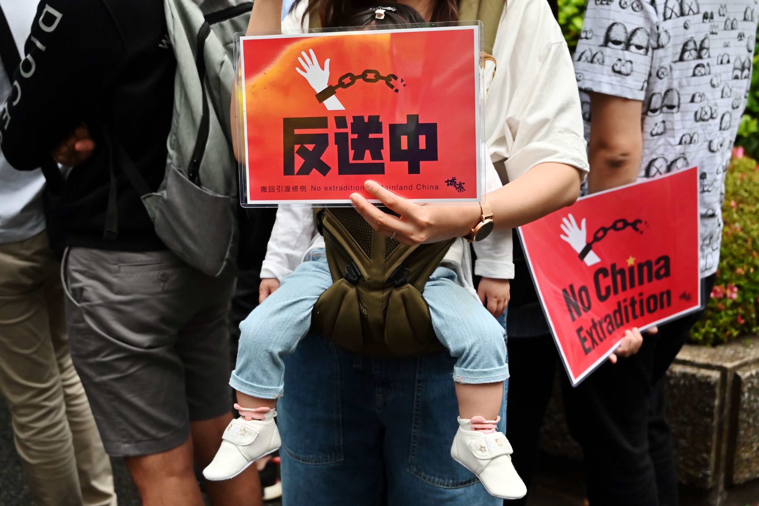 香港「反送中」遊行一名揹著幼兒的群眾舉起標語牌(9/6/2019)(圖片來源:AFP)