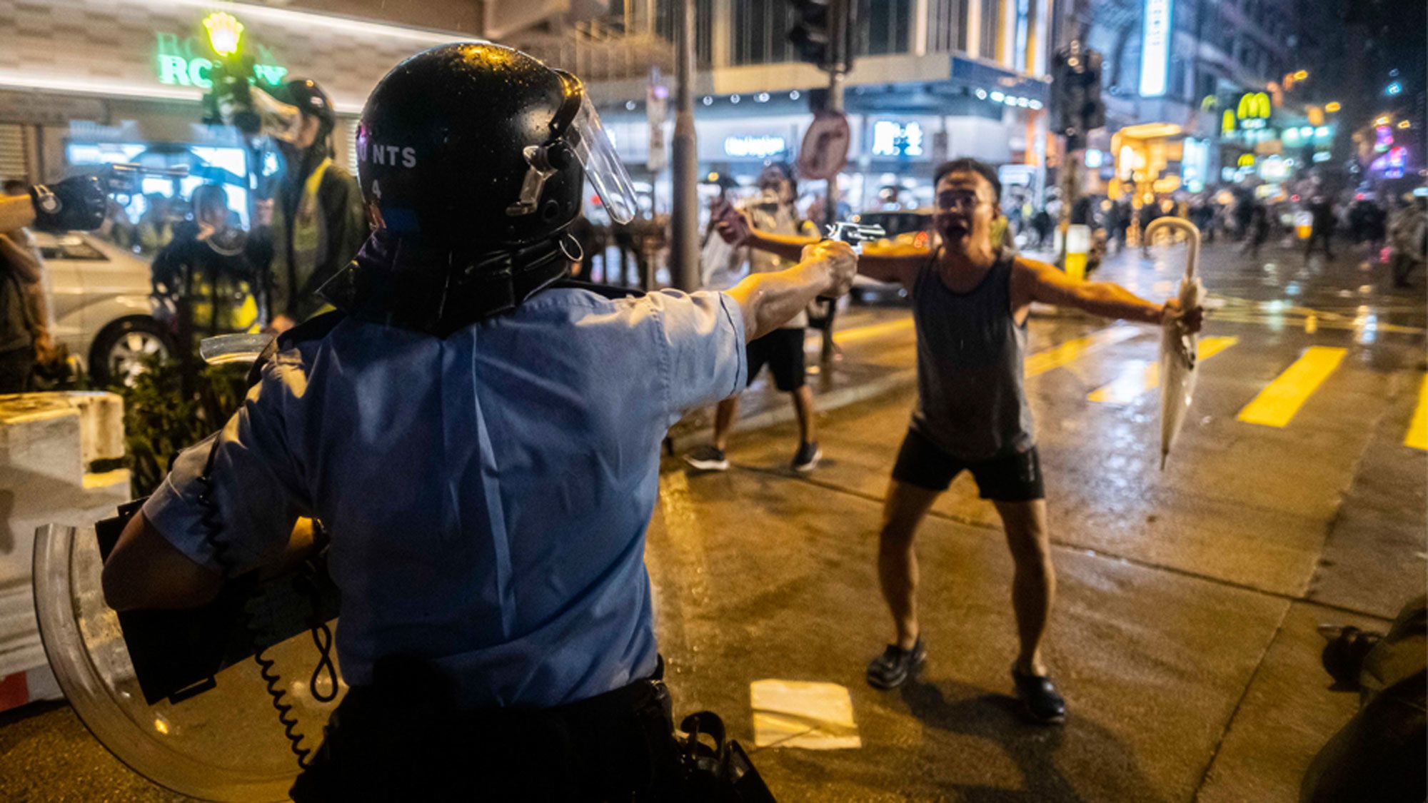 Man stands arms outstretched as police officer points gun at him