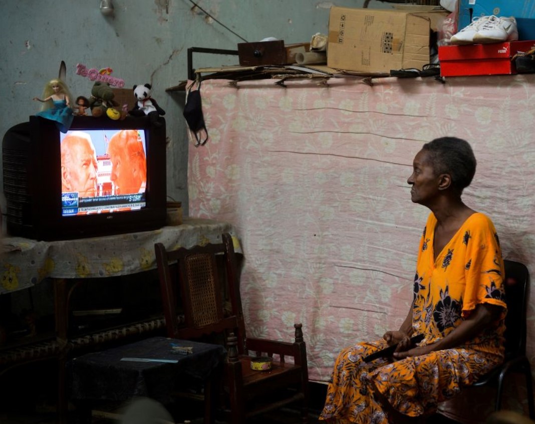 A woman in Havana watches a screen showing Donald Trump and Joe Biden graphic