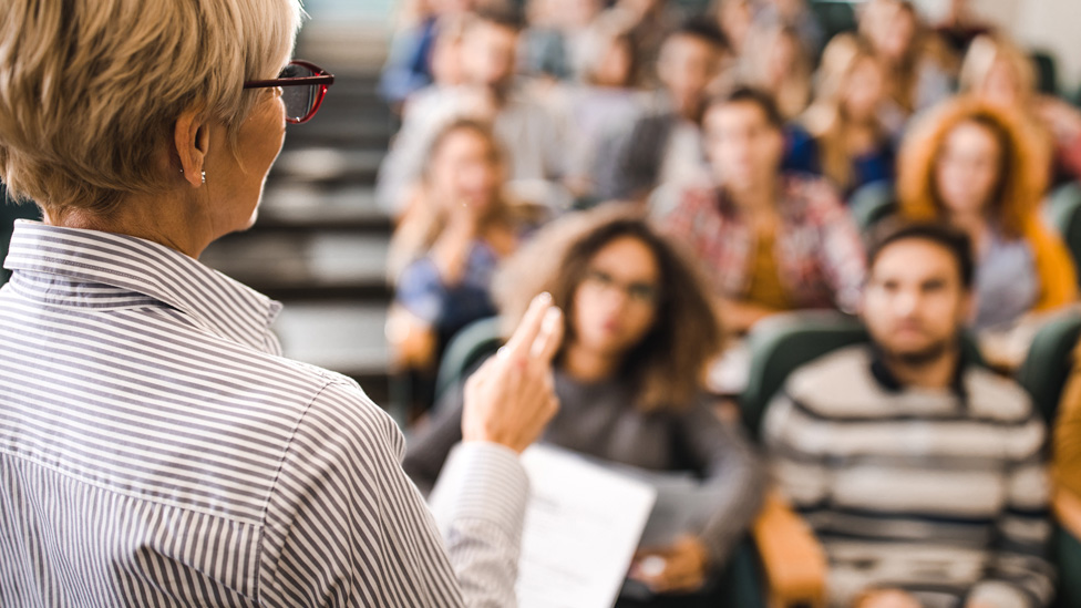 Woman lecturer standing with her back to the camera in front of students listening intently