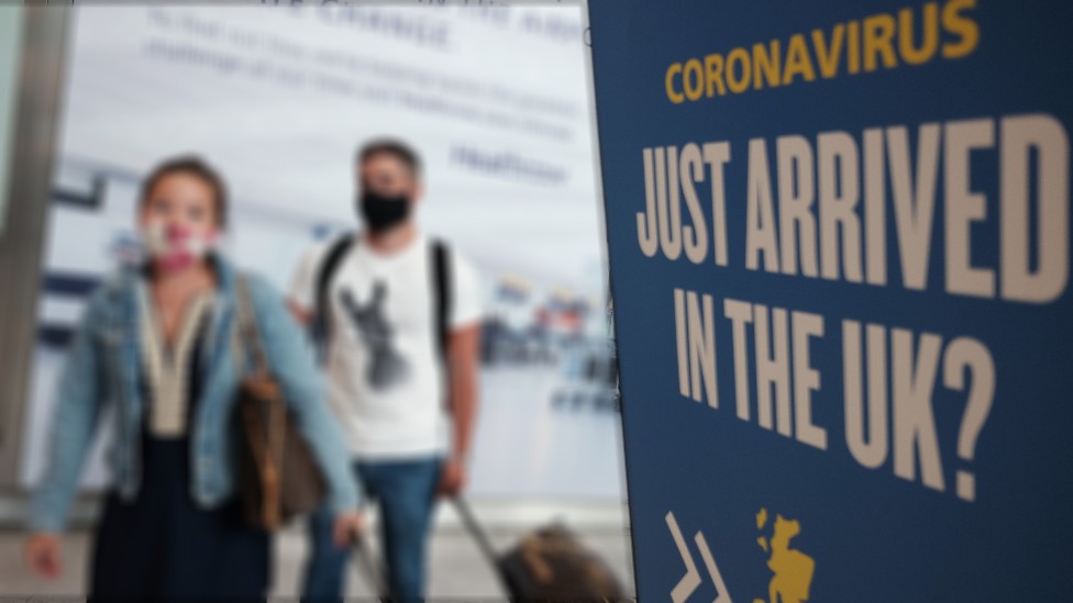 Two people in airport arrivals hall next to quarantine warning poster