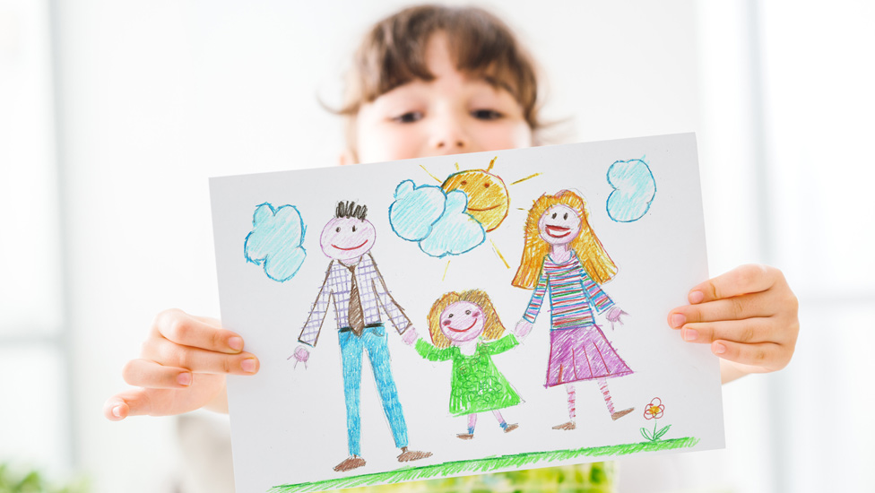 Image shows girl holding up a drawing of a family