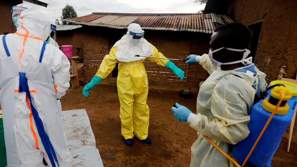 Kavota Mugisha Robert, a healthcare worker who volunteered in the Ebola response, decontaminates his colleague after he entered the house of 85-year-old woman