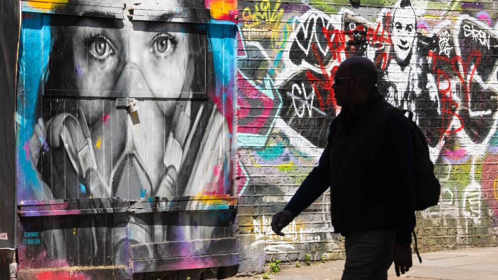 Pedestrian walks past a mural depicting a woman wearing a face mask