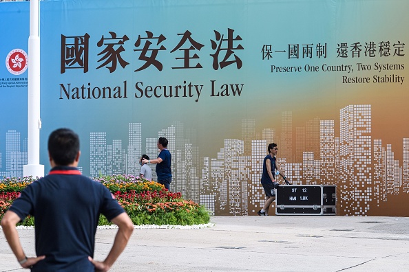 香港灣仔金紫荊廣場上給移交23週年慶典清理場地的工人望著宣傳《香港國安法》的巨型海報（1/7/2020）