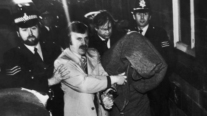 His head covered with a blanket, Peter Sutcliffe, is escorted into Dewsbury Magistrates Court to be charged with murder, 6 January 1981