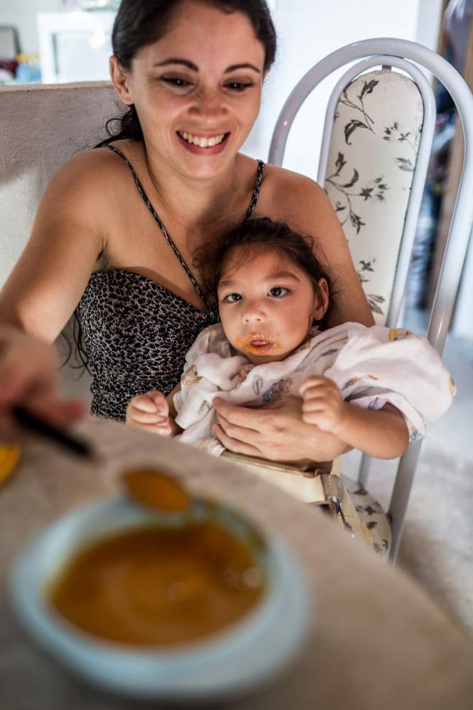 Cassiana dá comida para Melissa Vitória, uma batalha diária por causa da dificuldade de deglutição da filha