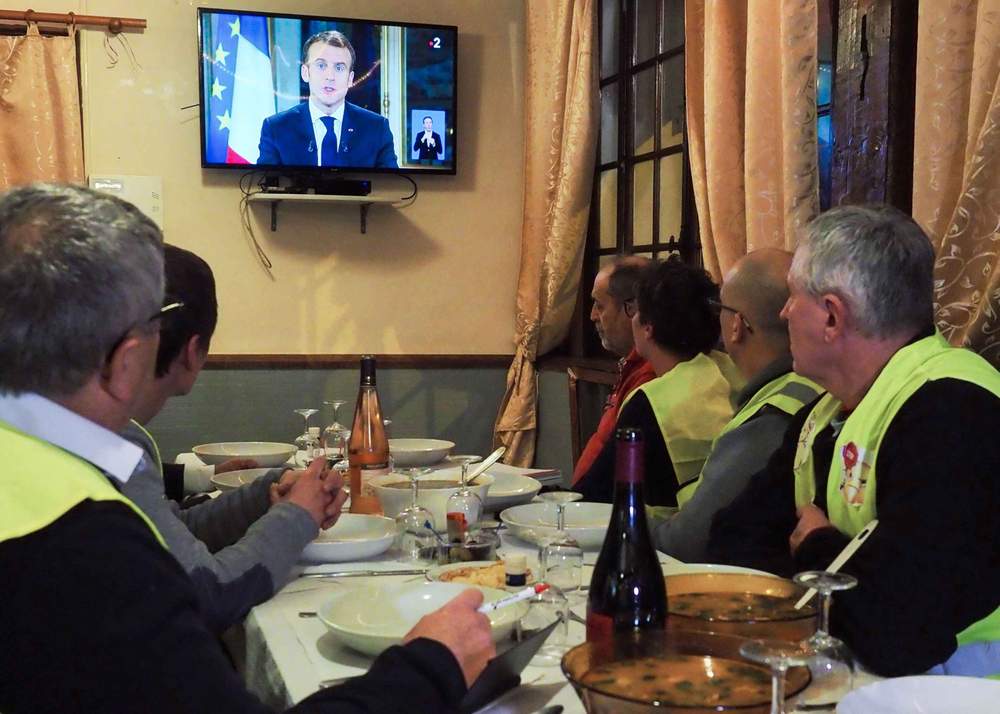 Protestors take notes as they watch French President Emmanuel Macron&#39;s speech on TV on 10 December 2018