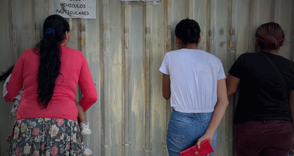 Tres mujeres de espalda mirando a través de un agujero en el muro de la cárcel de Apanteos